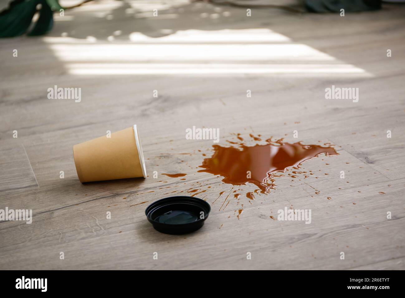 La tazza di carta di caffè è caduta su laminato, caffè versato sul pavimento. Foto Stock