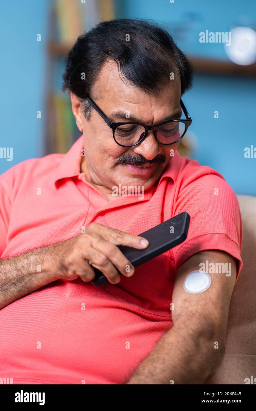 Immagine verticale dell'anziano che controlla il livello di glucosio toccando lo smartphone per monitorare il sensore a casa - concetto di assistenza sanitaria, tecnologia e. Foto Stock