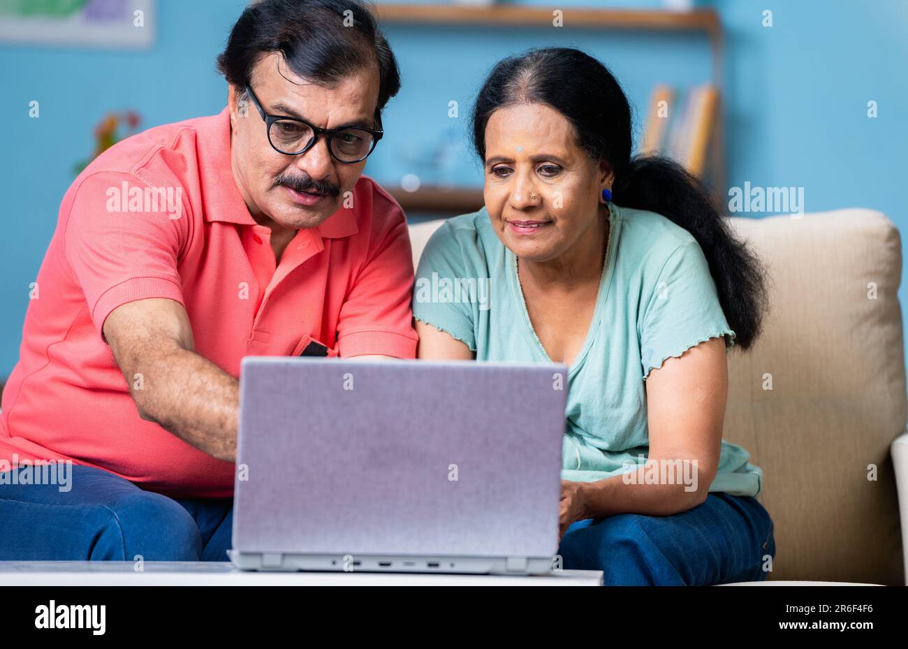 Coppia indiana senior discute guardando il notebook mentre si siede sul divano a casa - concetto di tecnologia, comunicazione e legame Foto Stock