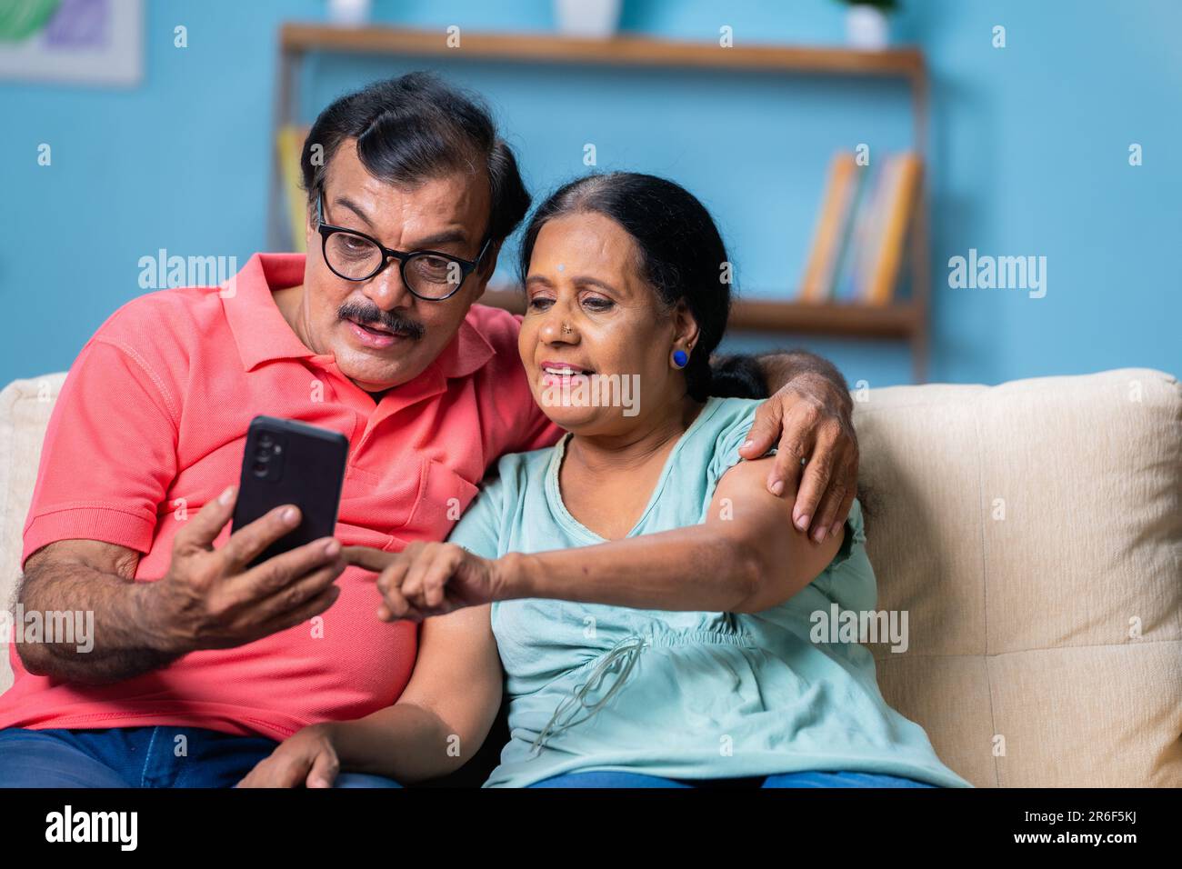 Felice coppia indiana senior utilizzando sul telefono cellulare mentre si siede sul divano a casa - concetto di social media e di pensione stili di vita e Internet Foto Stock