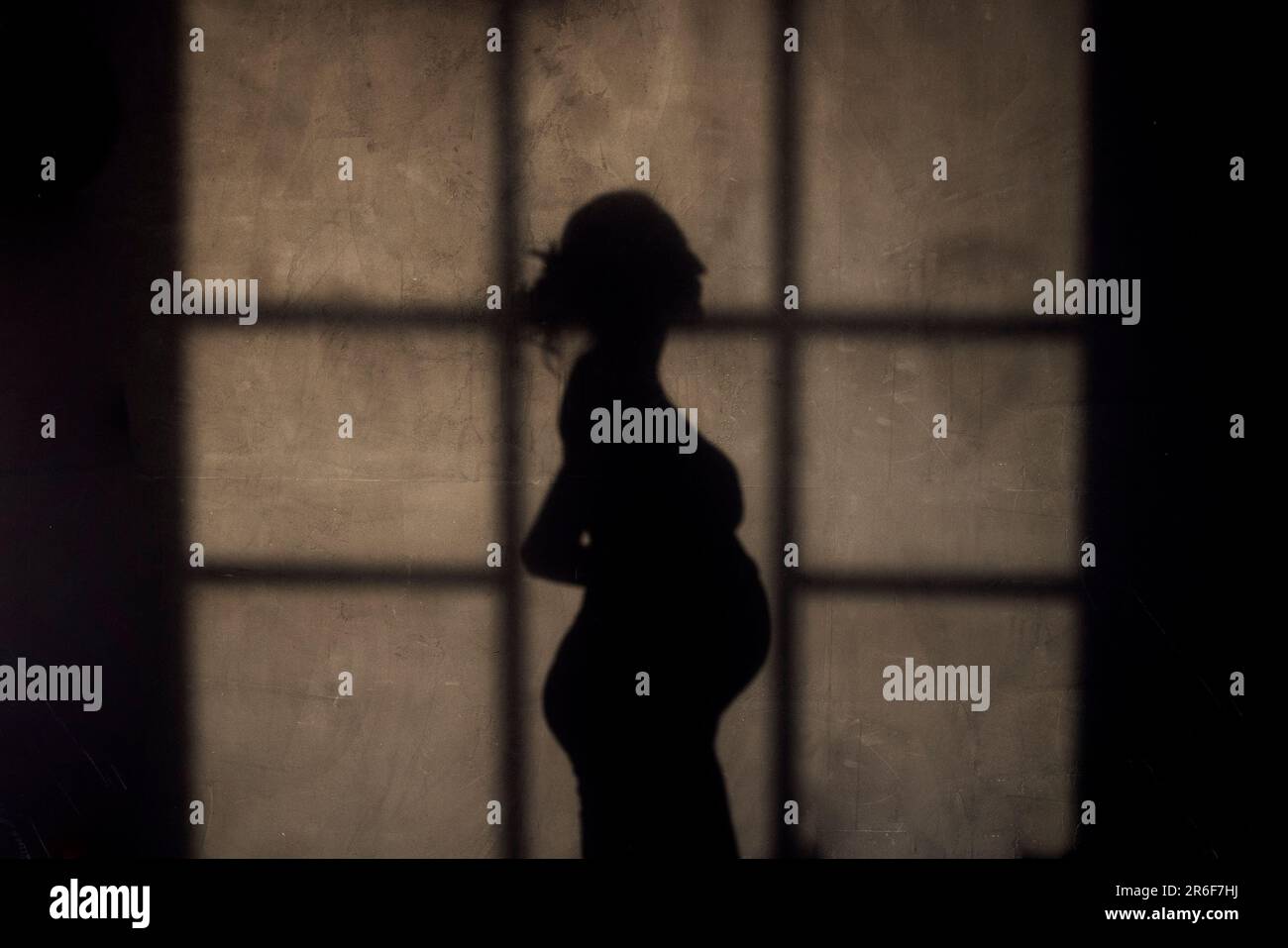 Shadow silhouette di una donna incinta contro una parete a trama grigia. Una donna che si aspetta un bambino in piedi lateralmente e toccare la pancia con le mani. Mothe Foto Stock