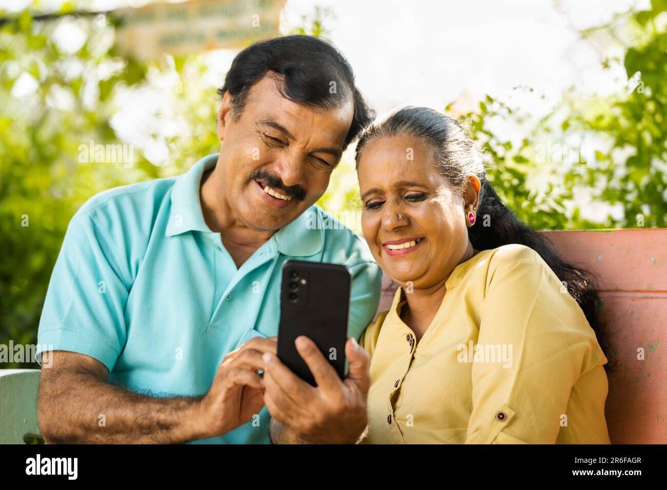 Ridere coppia anziana indiana mentre si guarda il telefono cellulare al parco - concetto di social media, tecnologia e stile di vita in pensione Foto Stock