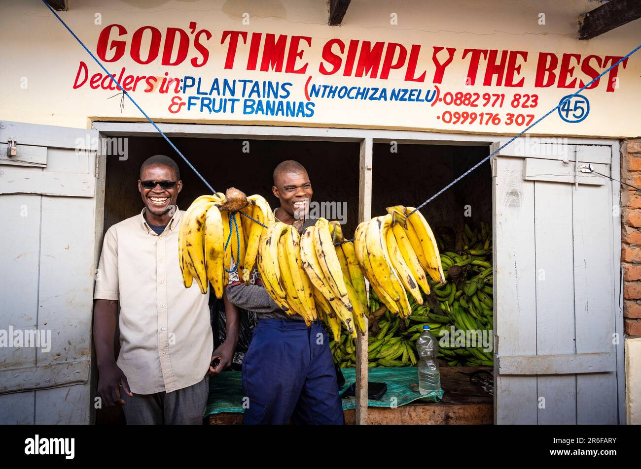 Due uomini stanno fuori dal loro negozio di banane nel mercato di Mzuzu, Malawi Foto Stock