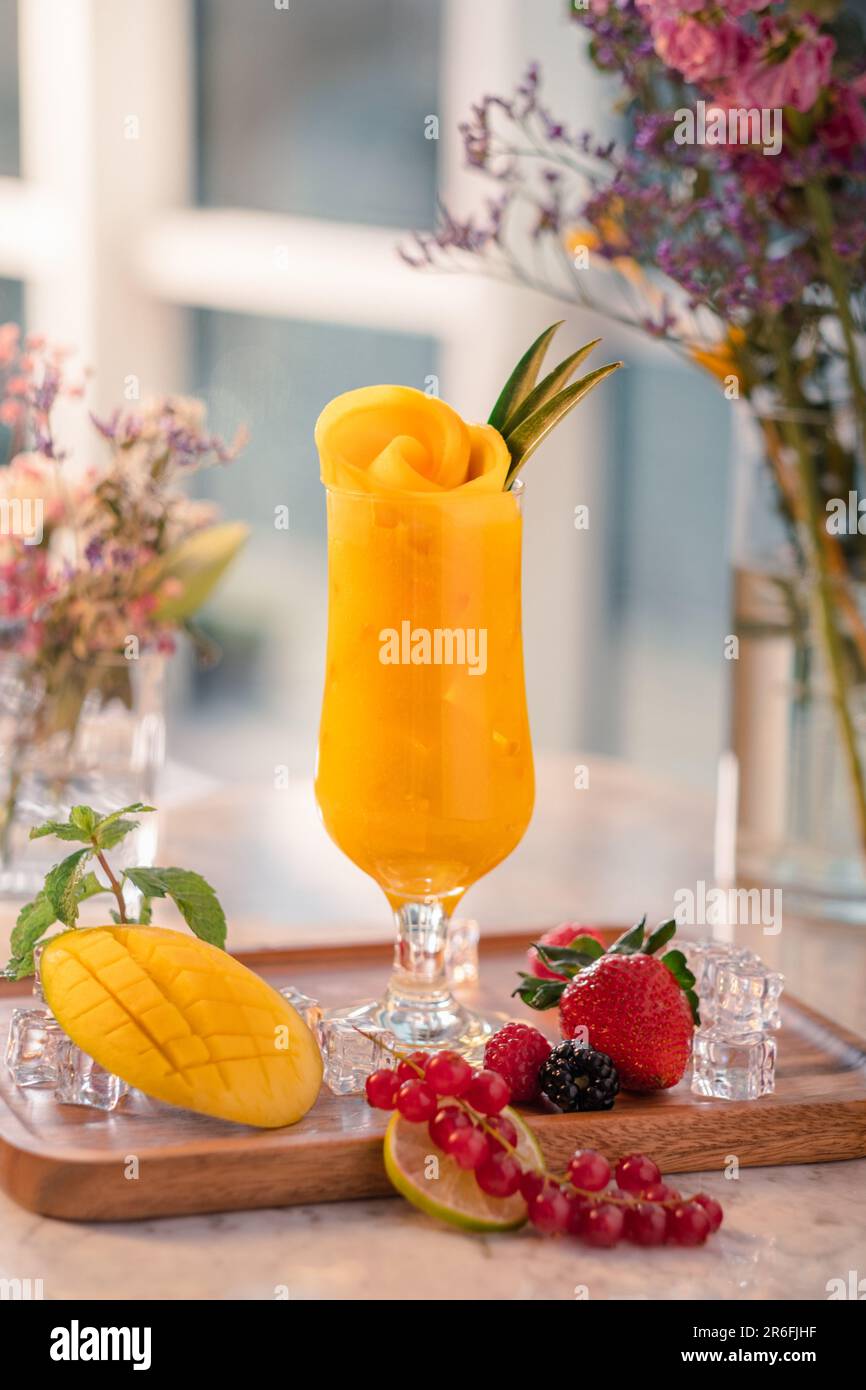 Un bicchiere di rinfrescante cocktail di frutta con una ciotola di fiori appena raccolti e qualche succosa fetta di frutta che lo circonda Foto Stock