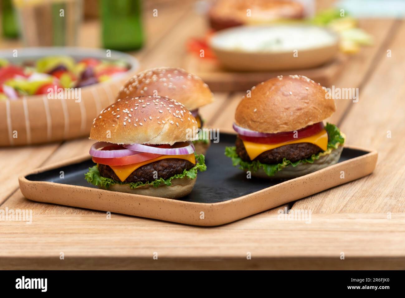 tre hamburger vegani su un piatto di legno con vari piatti vegani su un tavolo di legno Foto Stock