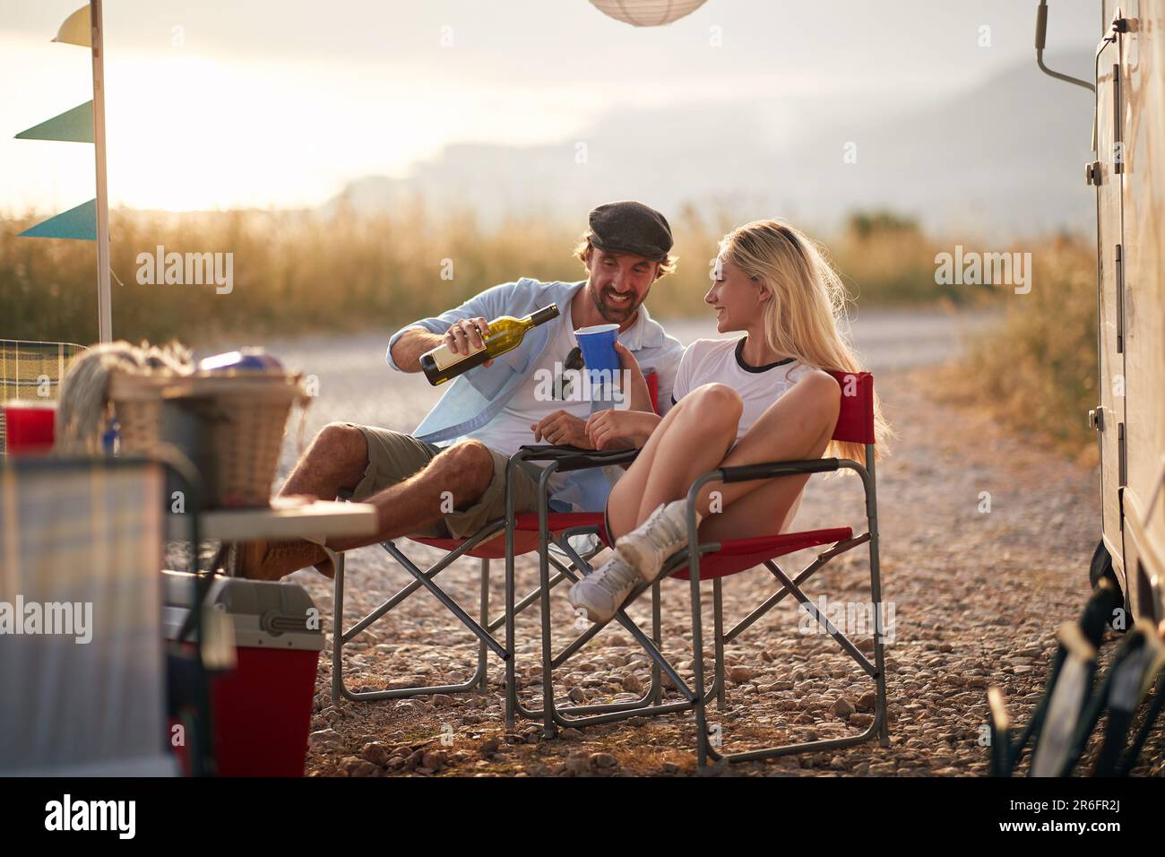 Coppia che si gode in estate campeggio con camper in natura, seduti e versare un bicchiere di vino. Divertimento, viaggio, convivenza, concetto di amore. Foto Stock