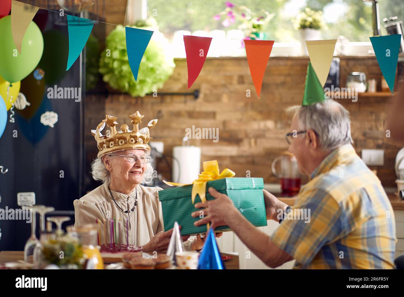 Coppia anziana che festeggia insieme, donna anziana di compleanno che riceve regalo di compleanno da suo marito seduto al tavolo della cena a casa. Celebrati Foto Stock