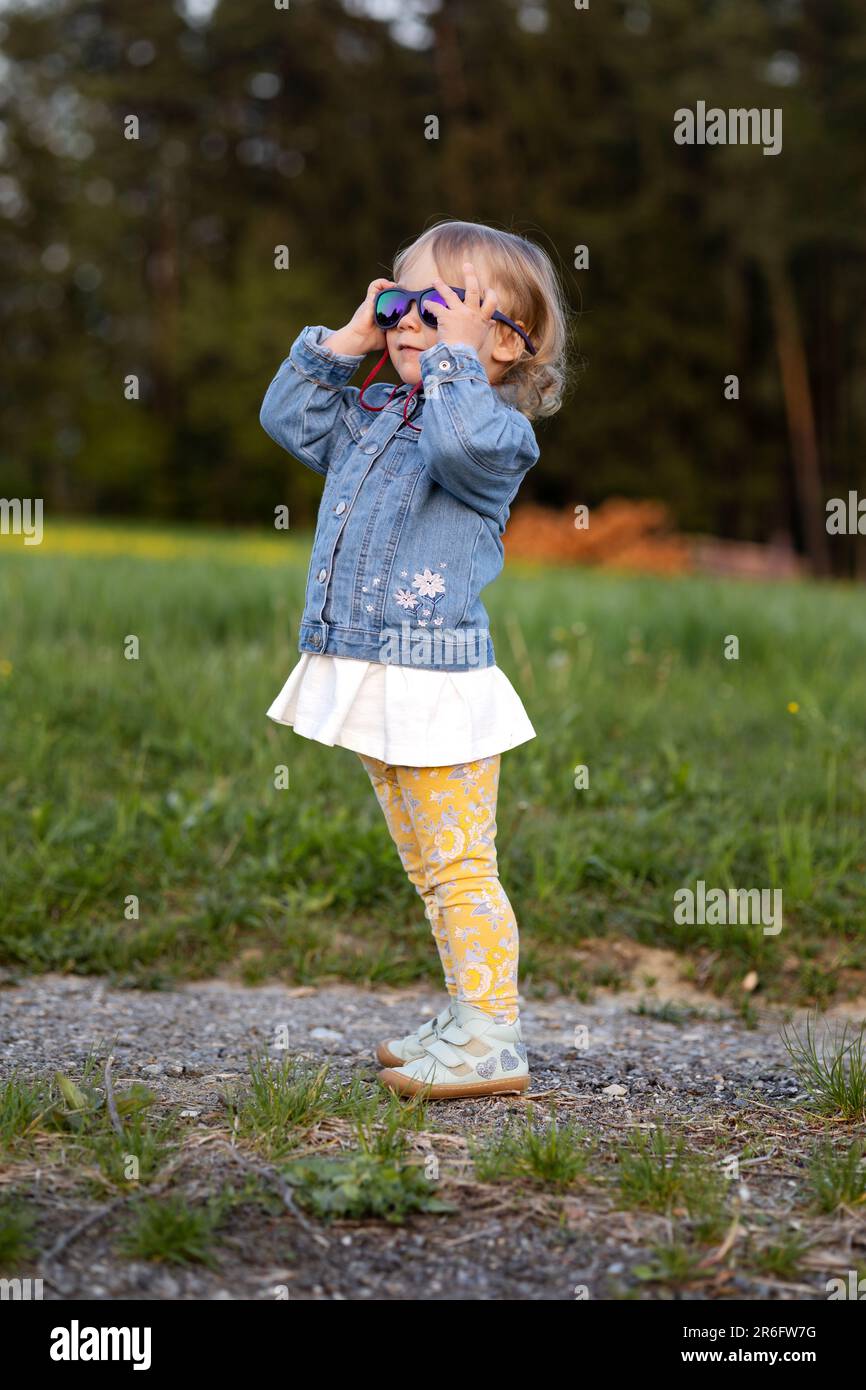 una bambina mette sugli occhiali da sole della sua mamma e si mostra Foto Stock