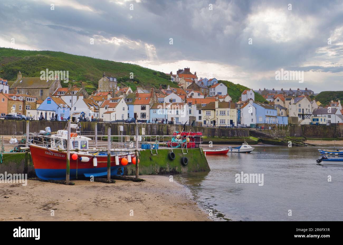 Passando nuvole di pioggia sul Porto di Staithes. La barca da pesca Three Sisters è un ricordo del patrimonio ittico della città. Foto Stock