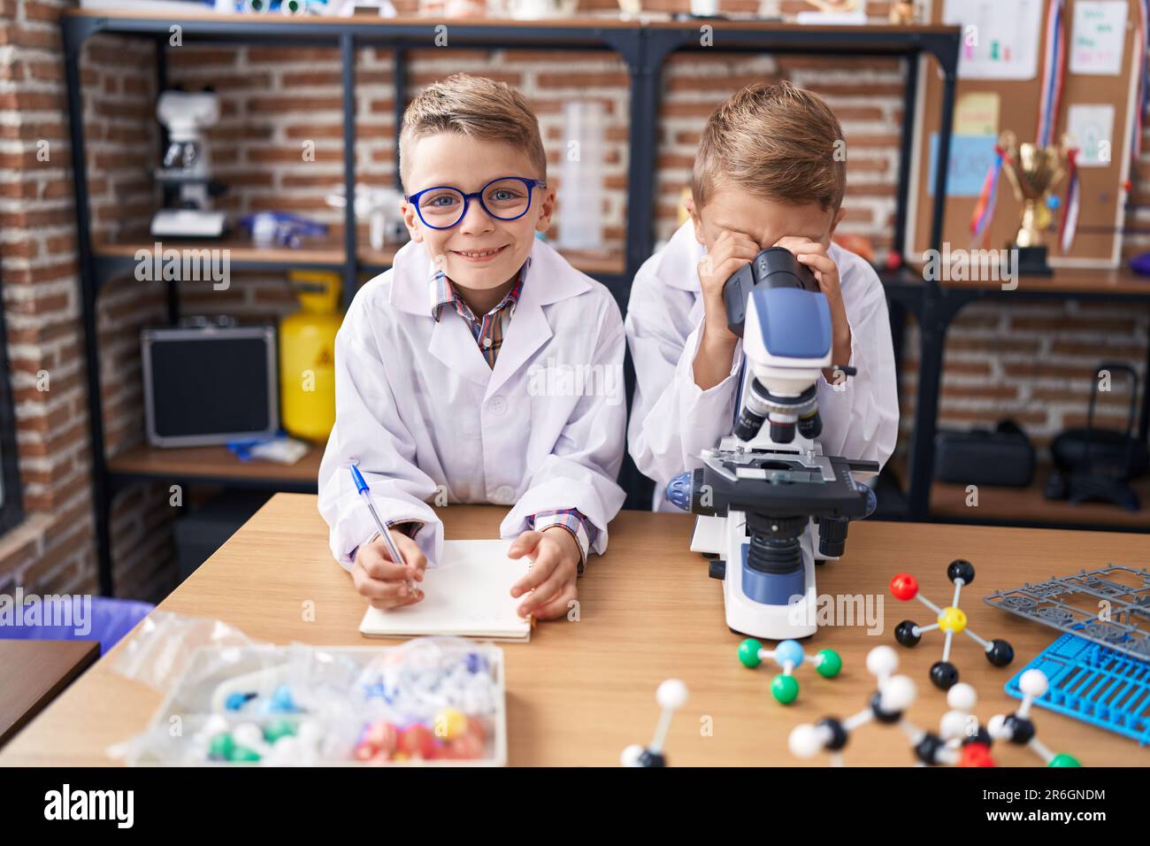 Adorabili ragazzi studenti che usano il microscopio per scrivere appunti in classe di laboratorio Foto Stock