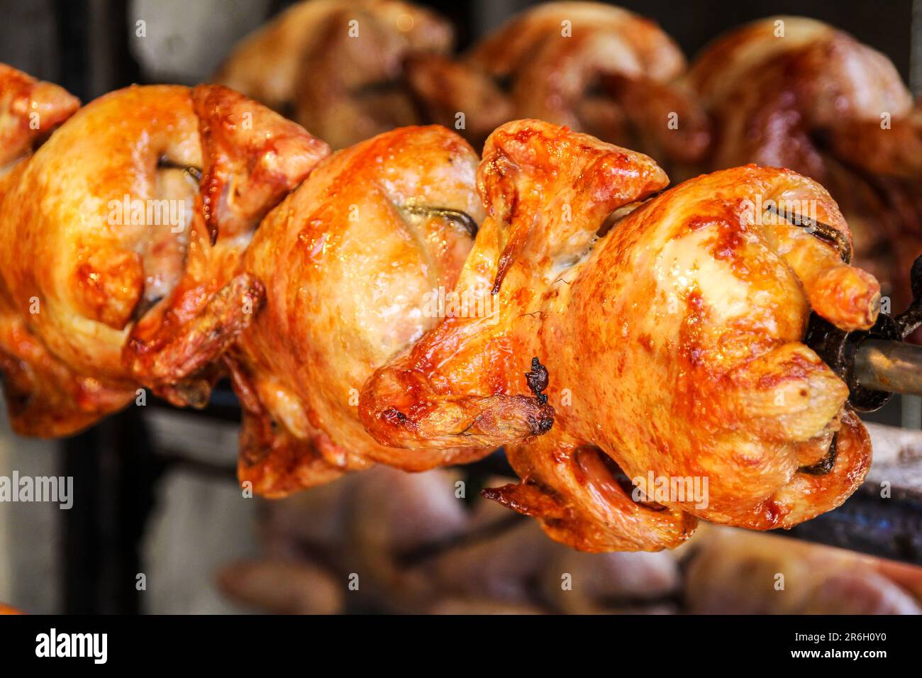 Primo piano di pollo intero arrosto con gustosa pelle dorata su una rotisserie in fila in uno stand di Street food Foto Stock