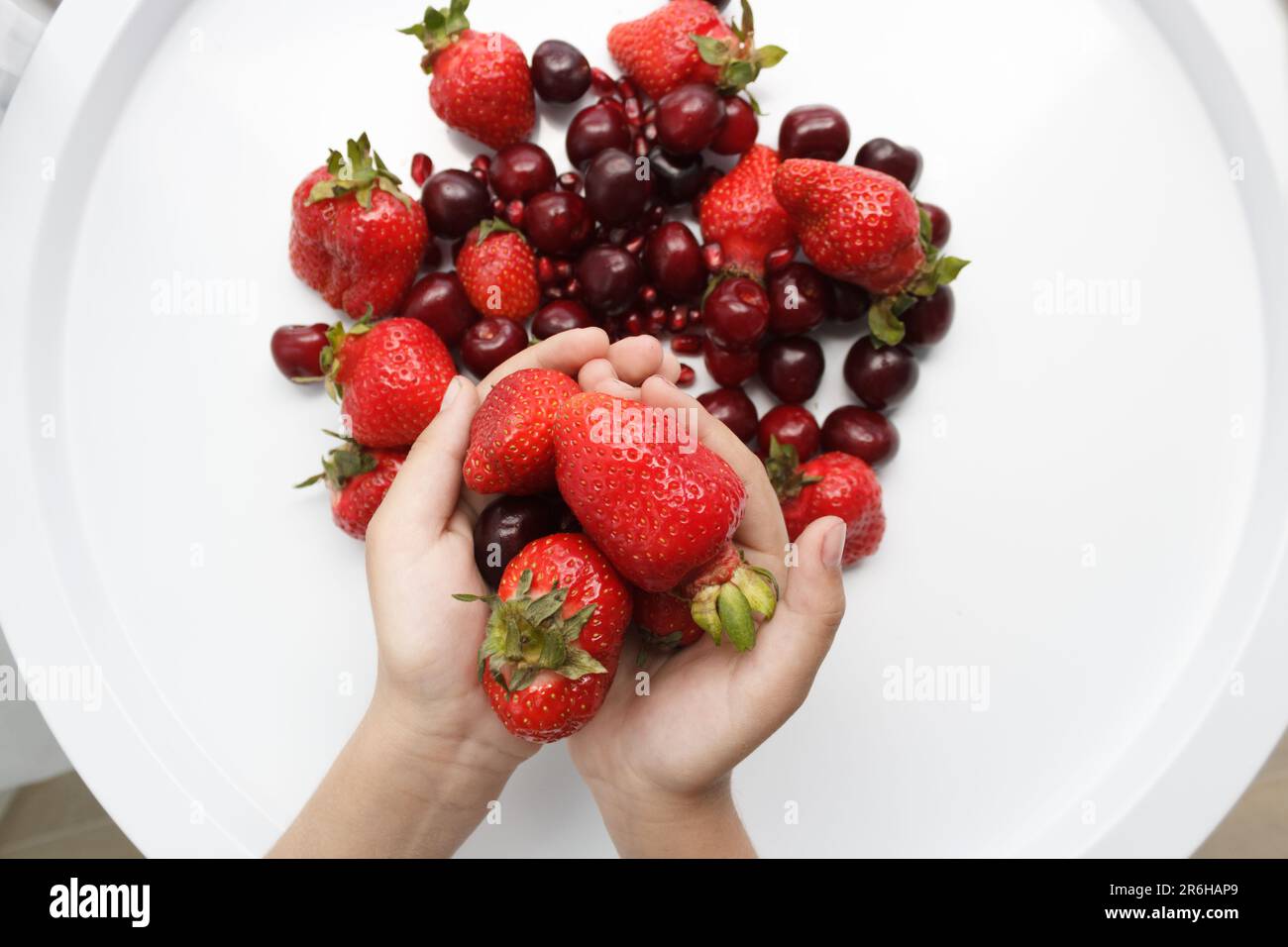 Le mani tengono grandi bacche rosse su un tavolo bianco con fragole, ciliegie e melograni. Foto Stock
