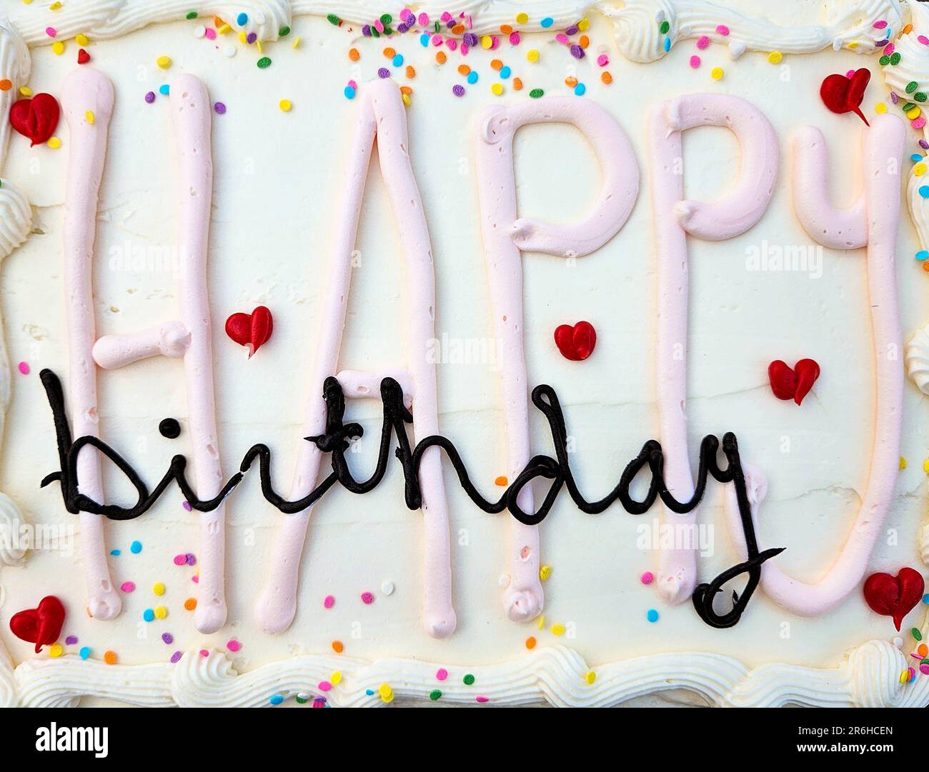 Buon compleanno testo sulla torta bianca glassa con cuori rossi e spruzzi colorati Foto Stock