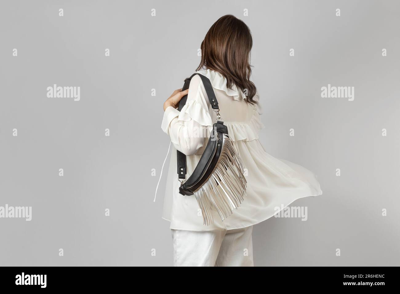 Donna bianca che indossa abiti bianchi e tracolla Borsa da cintura in pelle nera con frangia argentata decorativa su sfondo grigio Foto Stock
