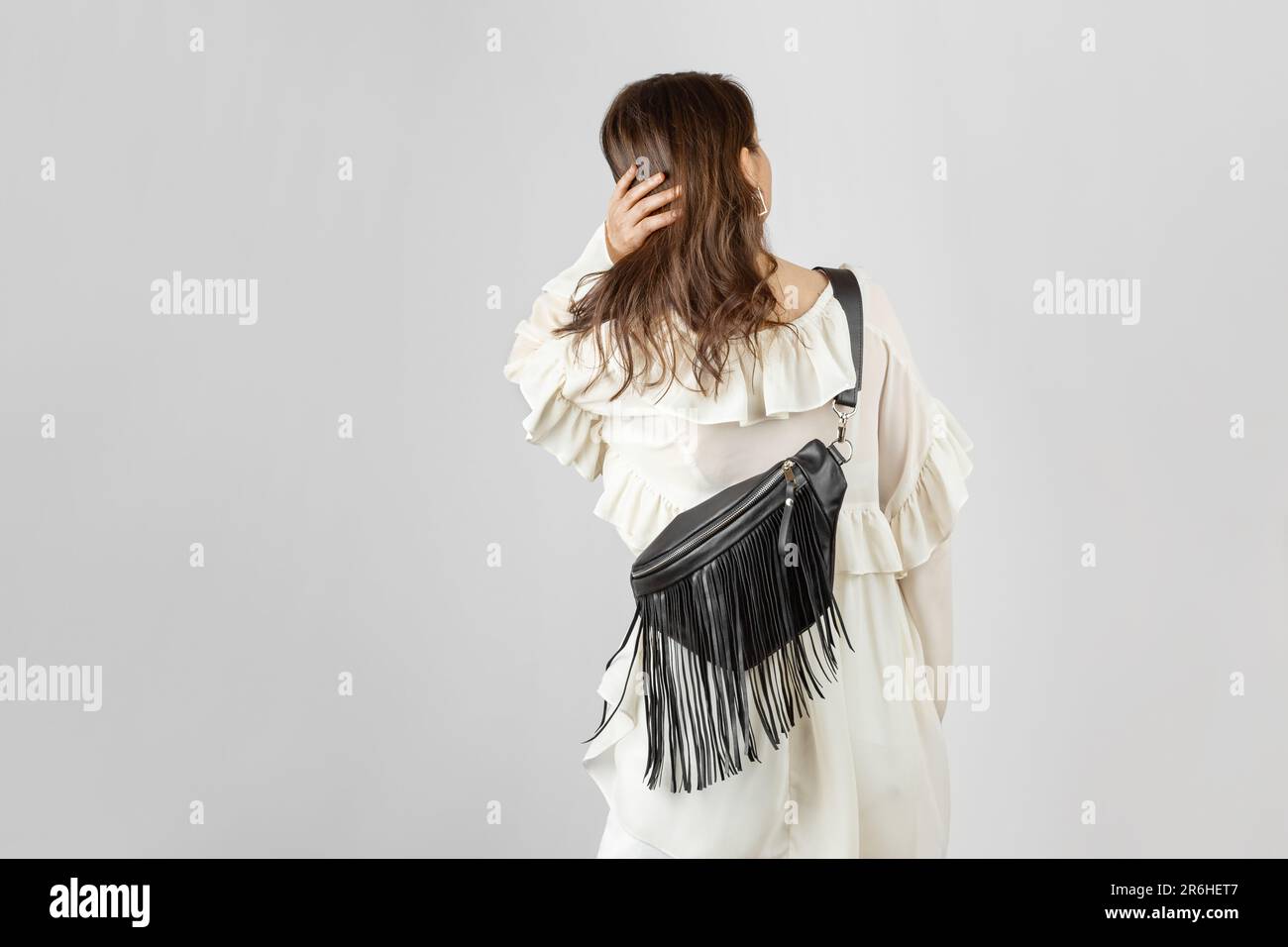 Donna bianca da dietro che indossa abiti bianchi e tracolla Borsa da cintura in pelle nera con frangia decorativa in stile Boho su sfondo grigio Foto Stock
