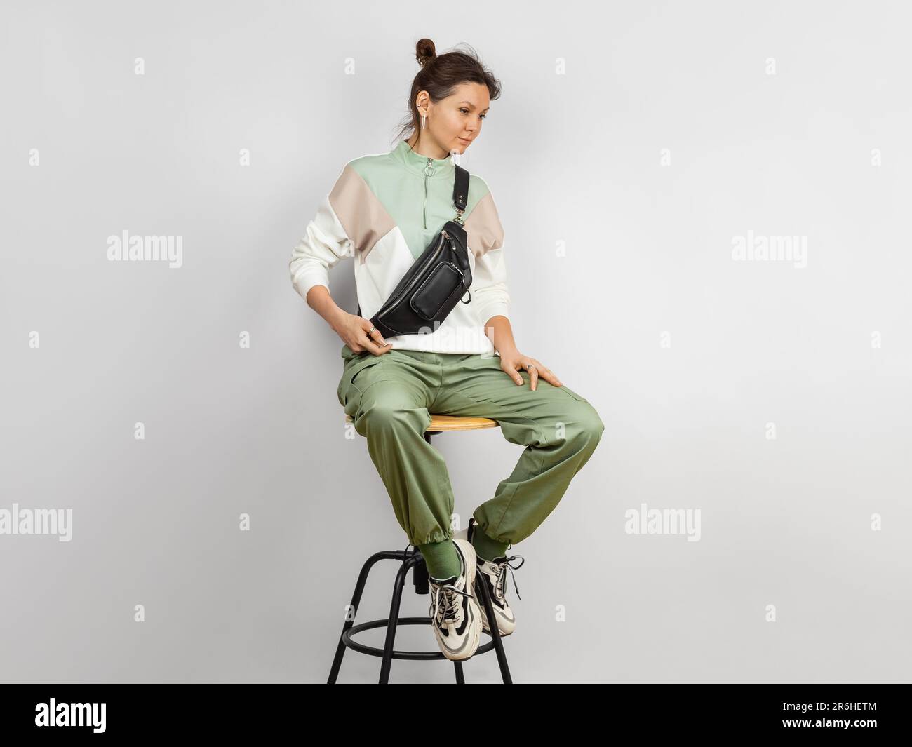 Ritratto del corpo a lunghezza intera di una donna che indossa la tracolla una borsa da cintura in pelle nera su sfondo grigio. Accessori in pelle fatti a mano Foto Stock