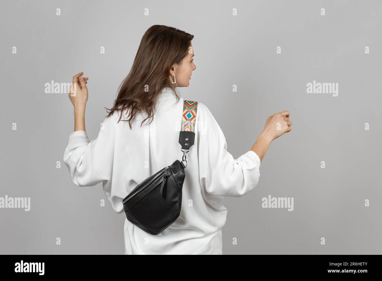 Donna bianca che indossa jeans bianchi, camicia e tracolla Borsa da cintura in pelle nera su sfondo grigio Foto Stock