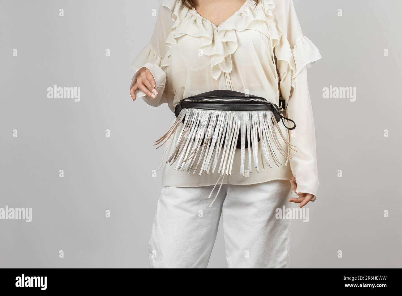 Donna bianca che indossa abiti bianchi e tracolla Borsa da cintura in pelle nera con frangia argentata decorativa su sfondo grigio Foto Stock