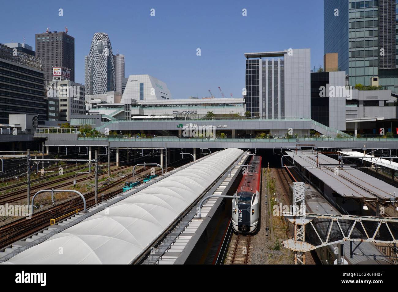 La vista frontale dei binari ferroviari che entrano nella massiccia ed enorme stazione ferroviaria di Shinjuku di Tokyo e' circondata da alti edifici di uffici e dai treni della Japan Rail Foto Stock