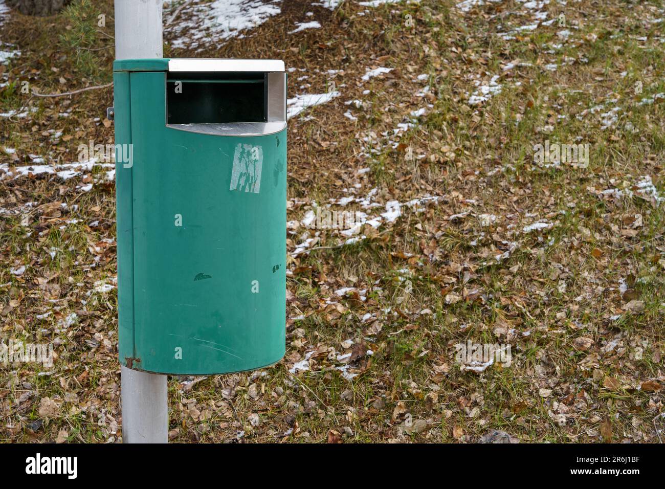 Cestino verde può su palo metallico con erba e neve sullo sfondo Foto Stock