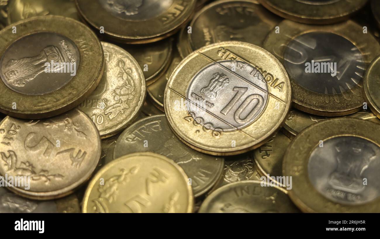 primo piano di una vecchia moneta indiana d'oro e d'argento 10 rupie in una collezione di autentiche monete da dieci e cinque rupie in pile sparse Foto Stock