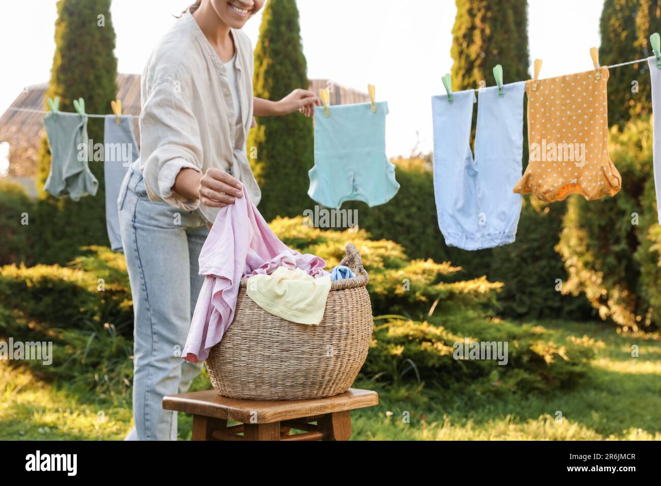 Donna sorridente appendere vestiti del bambino con i clothespins sulla linea di lavaggio per asciugare nel cortile posteriore, primo piano Foto Stock