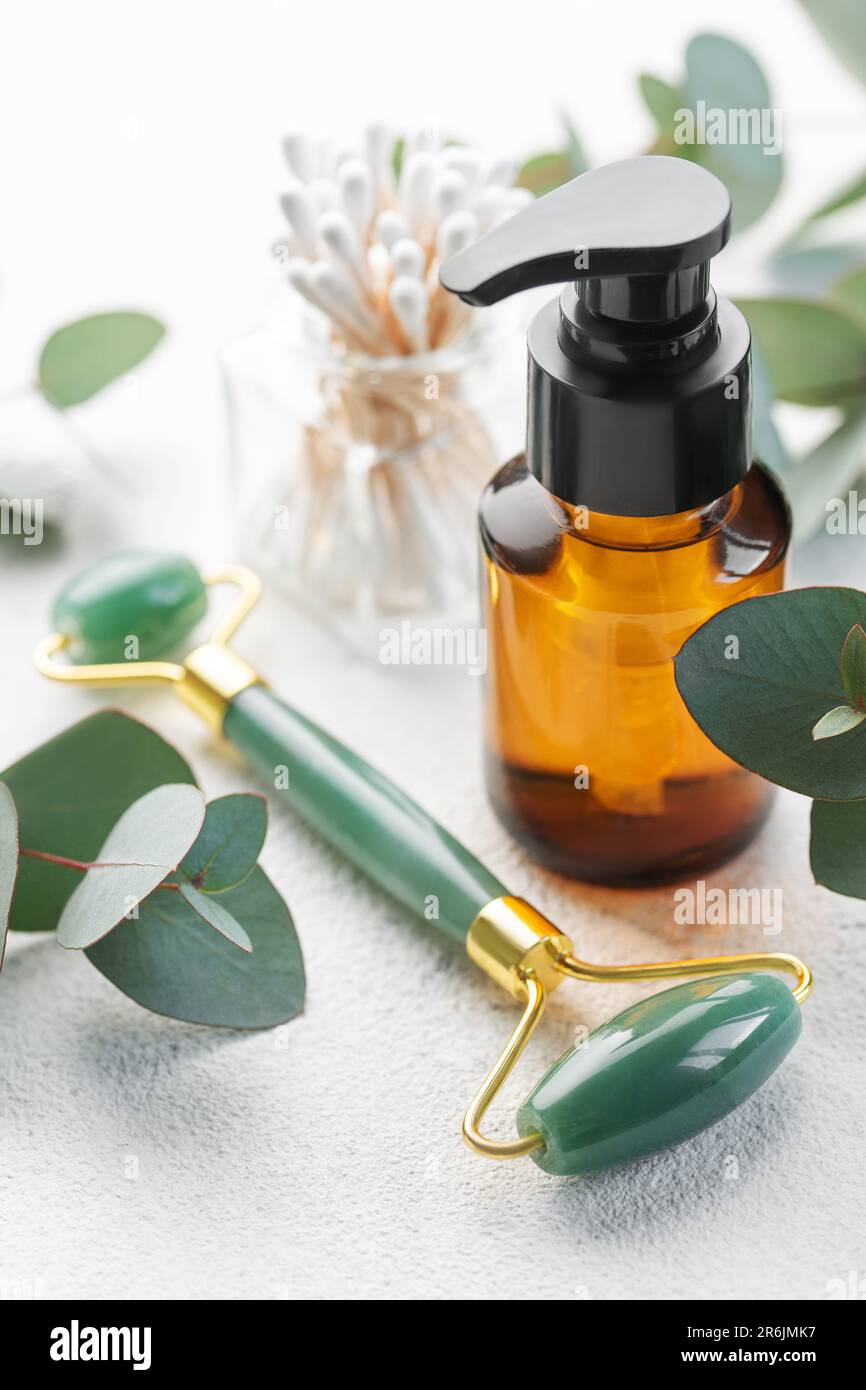 Cura naturale della pelle e aromaterapia con bottiglia di olio essenziale di eucalipto, rullo di giada di bellezza, gua sha su fondo di cemento. Spa, benessere, massaggi e Foto Stock