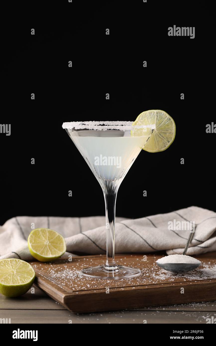 Martini bicchiere di cocktail rinfrescante con lime e zucchero su tavolo di legno su sfondo nero Foto Stock