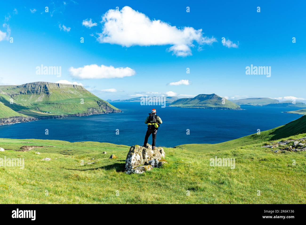 Escursionista in cima alla roccia che contempla il fiordo in estate, Nordradalur, Streymoy Island, Faroe Islands, Danimarca, Europa Foto Stock