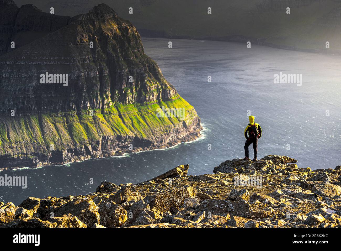 Un uomo che ammira le maestose scogliere lungo un fiordo in cima alla montagna durante un'escursione, Vidoy Island, Faroe Islands, Denmark, Europe Foto Stock