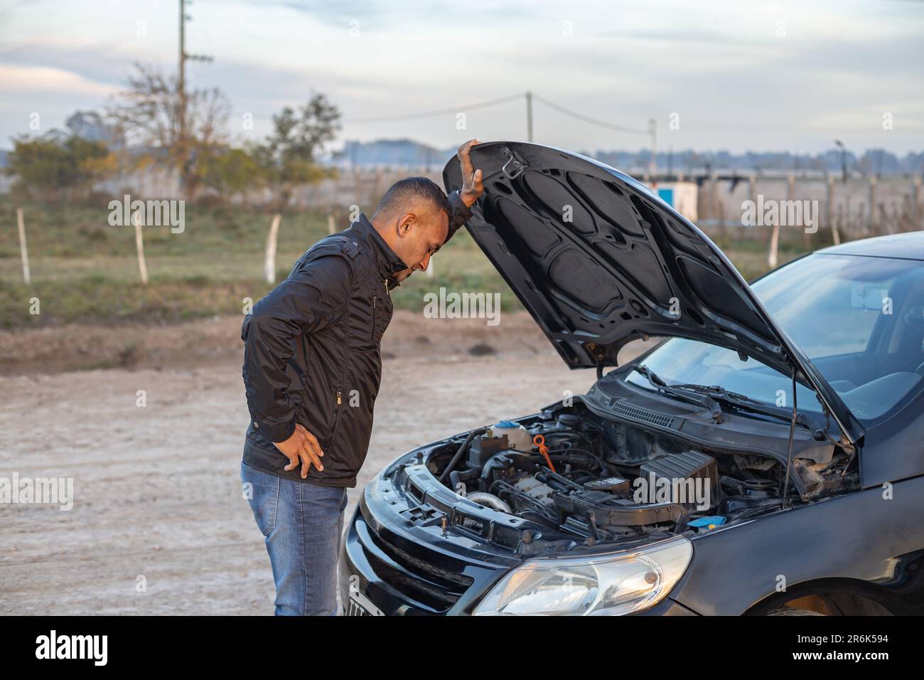 Giovane Latino che guarda il motore della sua auto rotta sul lato della strada. Foto Stock