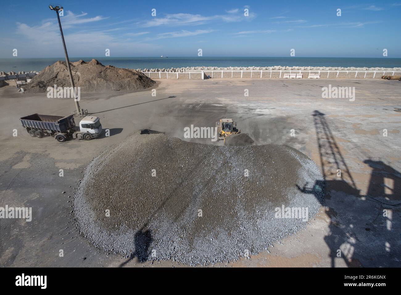 Cemento in movimento: Escavatore al lavoro nel porto di Laayoune, nel sud del Marocco Foto Stock