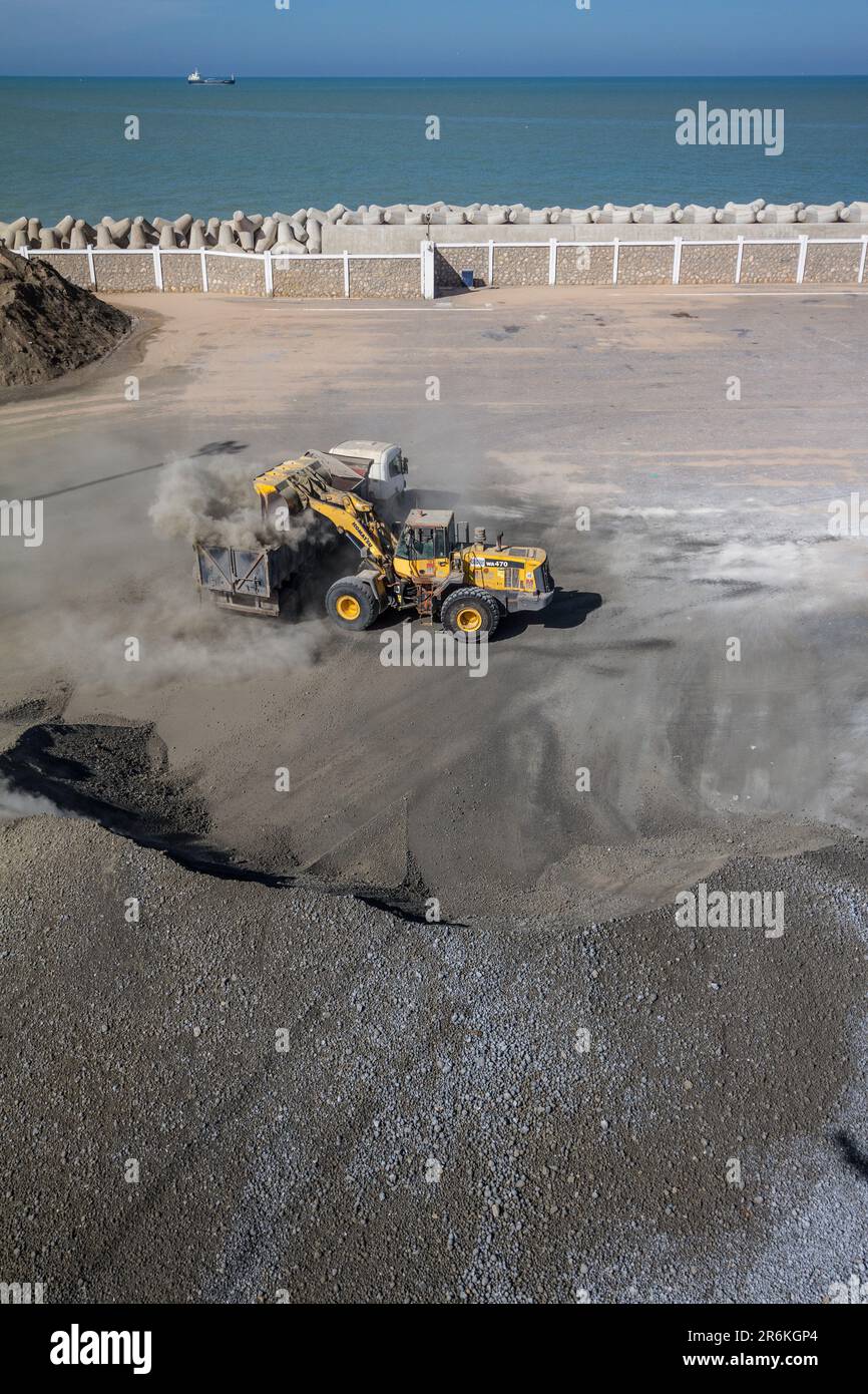 Essential Cargo: Escavatore che carica il cemento nel dumper presso il porto di Laayoune in Marocco Foto Stock