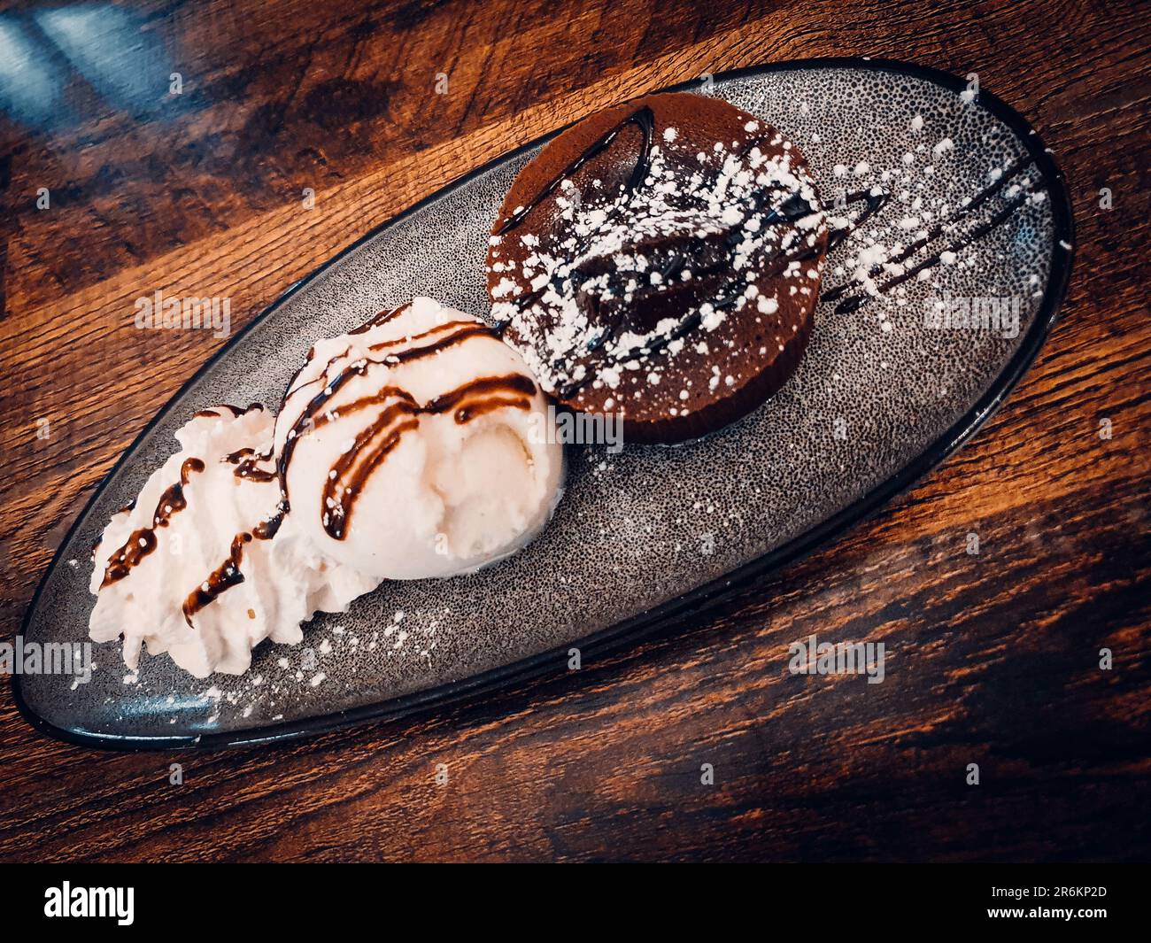 Torta al cioccolato servita con gelato alla vanila su un elegante piatto su un tavolo di legno Foto Stock