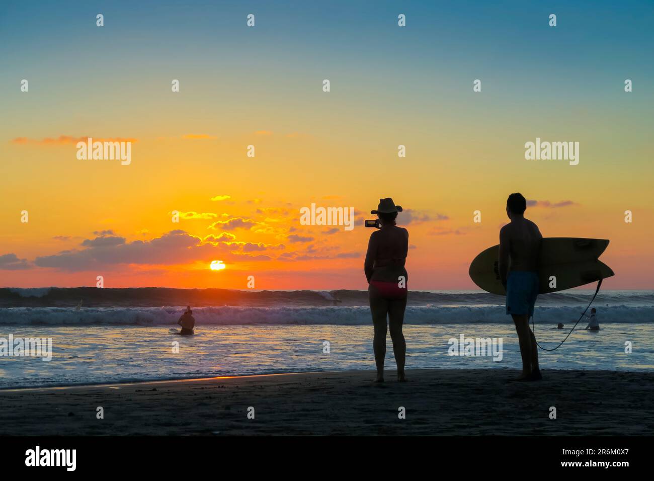 Surfista e donna fotografando il tramonto con smartphone sulla popolare spiaggia di Guiones, Playa Guiones, Nosara, Guanacaste, Costa Rica, America Centrale Foto Stock