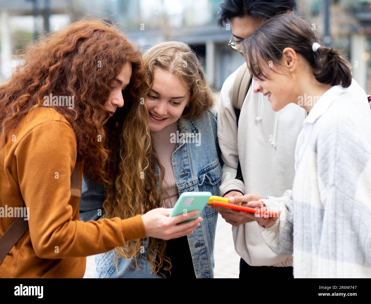 Gruppo di amici adolescenti che si trovano a guardare lo smartphone in una città. Giovani Millennial che utilizzano la tecnologia Foto Stock