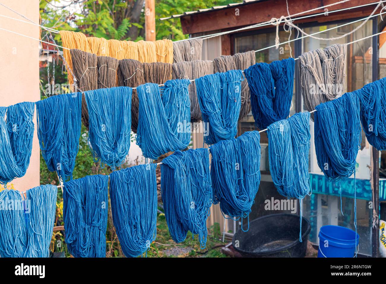Matasse di filo tinto a mano nelle sfumature di blu, oro e taupe appendono su linee di corda per asciugare all'aperto al negozio di tessitura Trujillo a Chimayo, New Mexico. Foto Stock