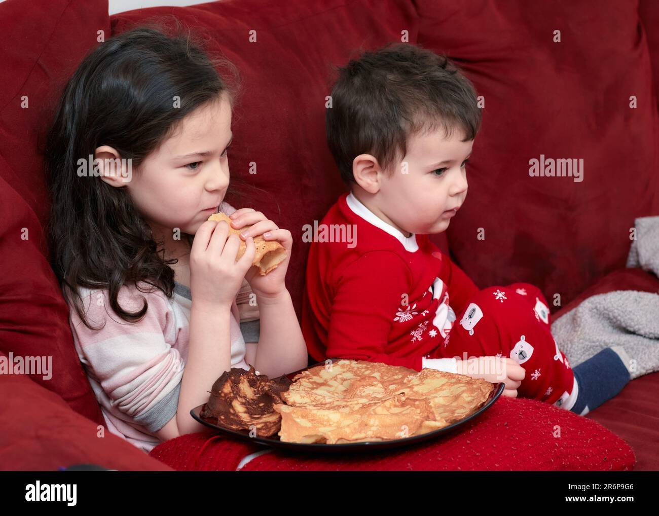 fratello e sorella che hanno spuntini sul divano Foto Stock