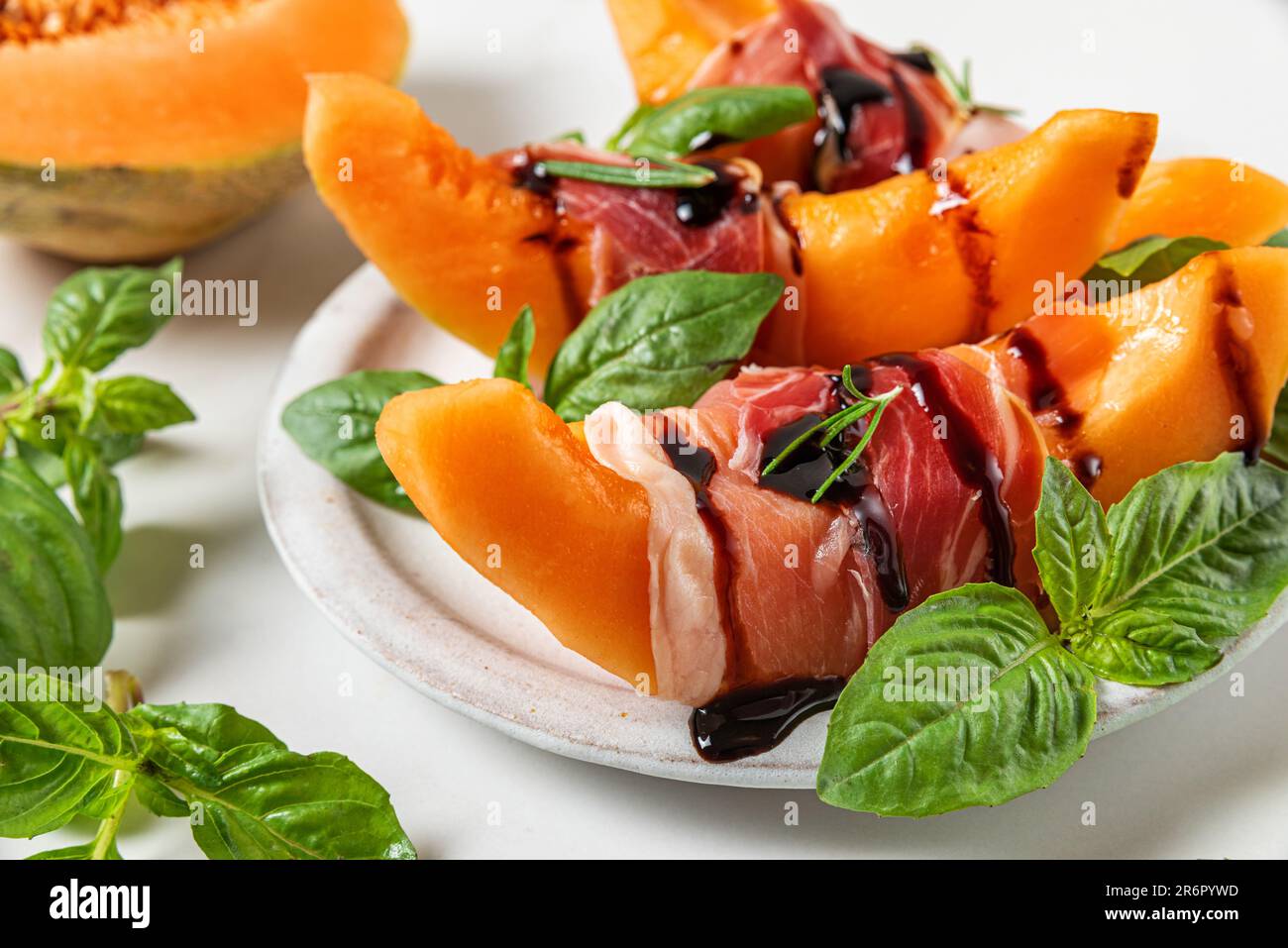 Prosciutto con fettine di melone cantaloupe, salsa all'aceto balsamico e basilico in un piatto su fondo bianco Foto Stock