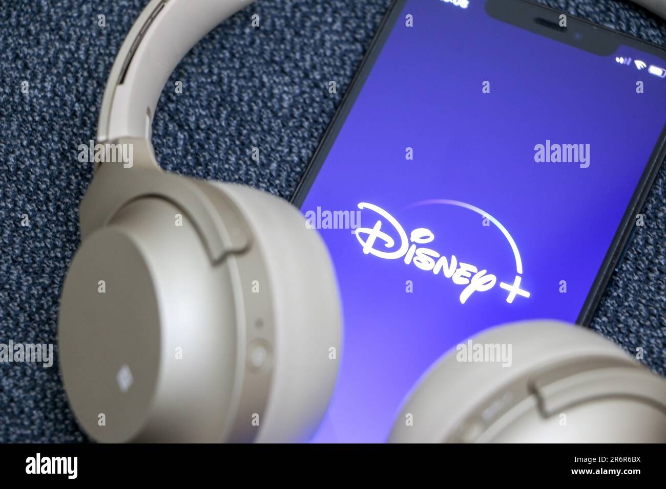 Guardando Disney Plus sullo smartphone, il logo Disney + sullo schermo, le cuffie dorate, il concetto di streaming online, Disney Plus è la massi di Disney Foto Stock