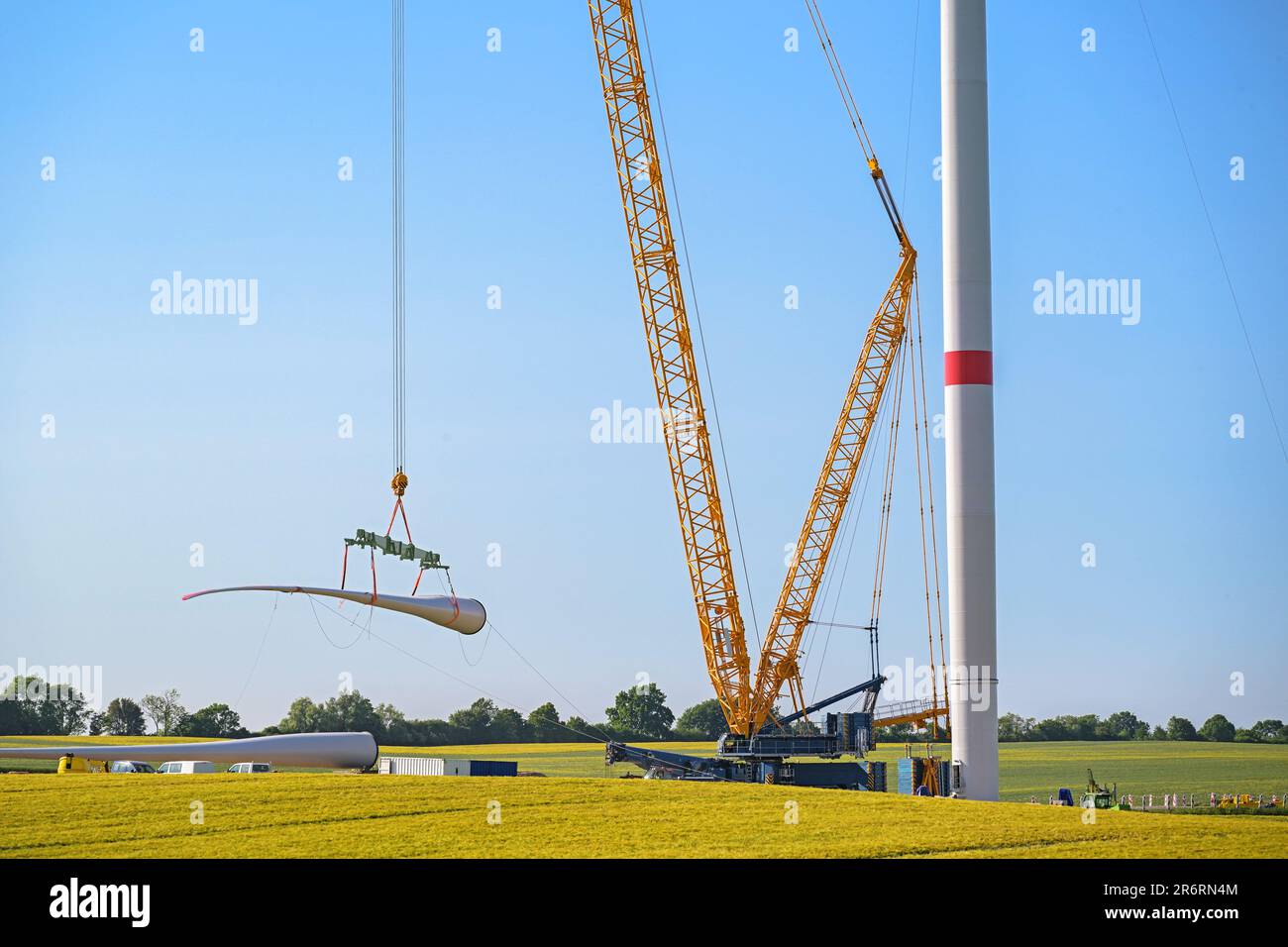 Gru gigante che solleva una pala di turbina eolica per installarla sulla torre, cantiere di costruzione industriale pesante, concetto di elettricità, energia rinnovabile e. Foto Stock
