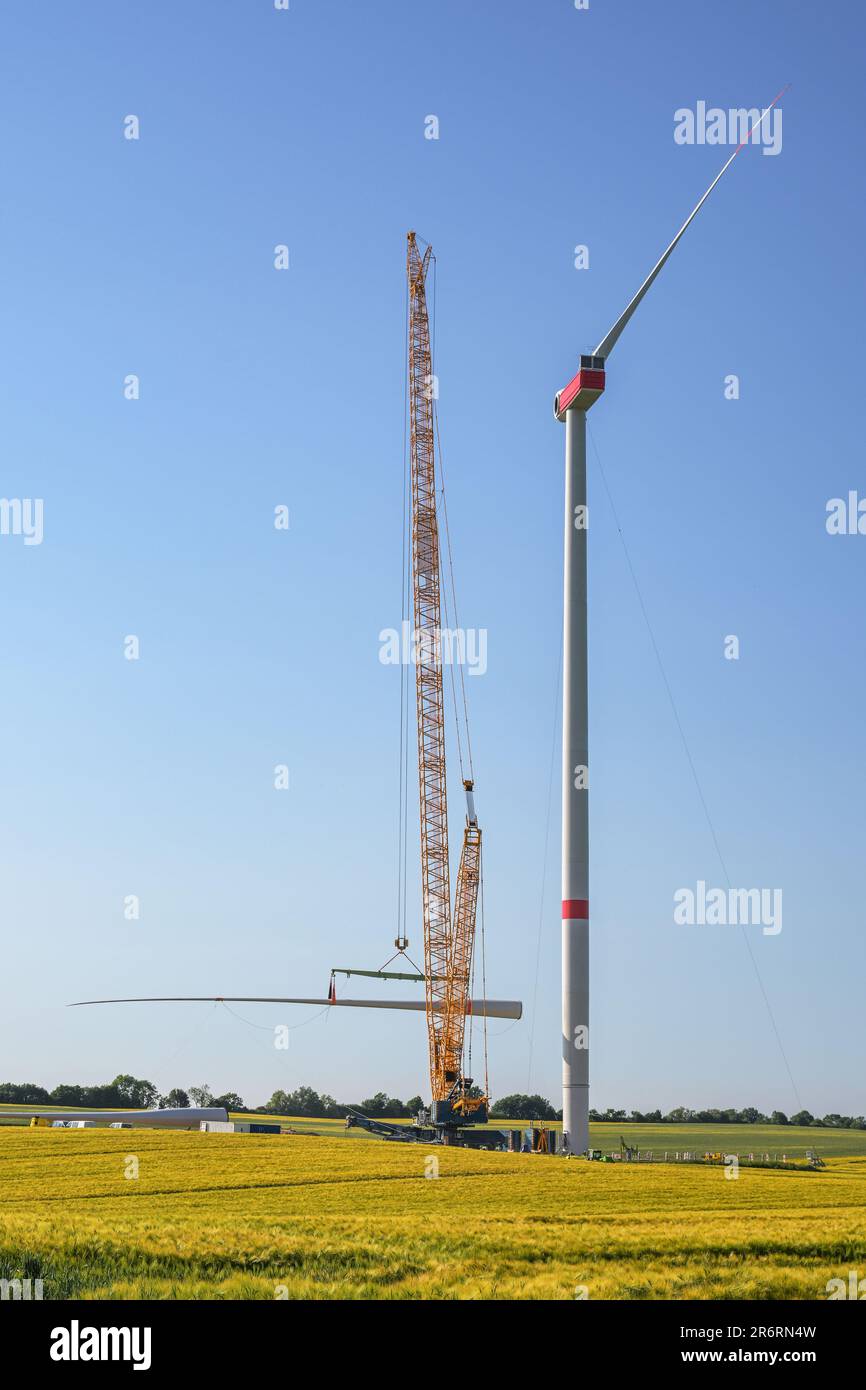 Cantiere gigantesco per una turbina eolica, la gru solleva la seconda pala per installarla sulla torre, industria pesante per le energie rinnovabili in un r Foto Stock