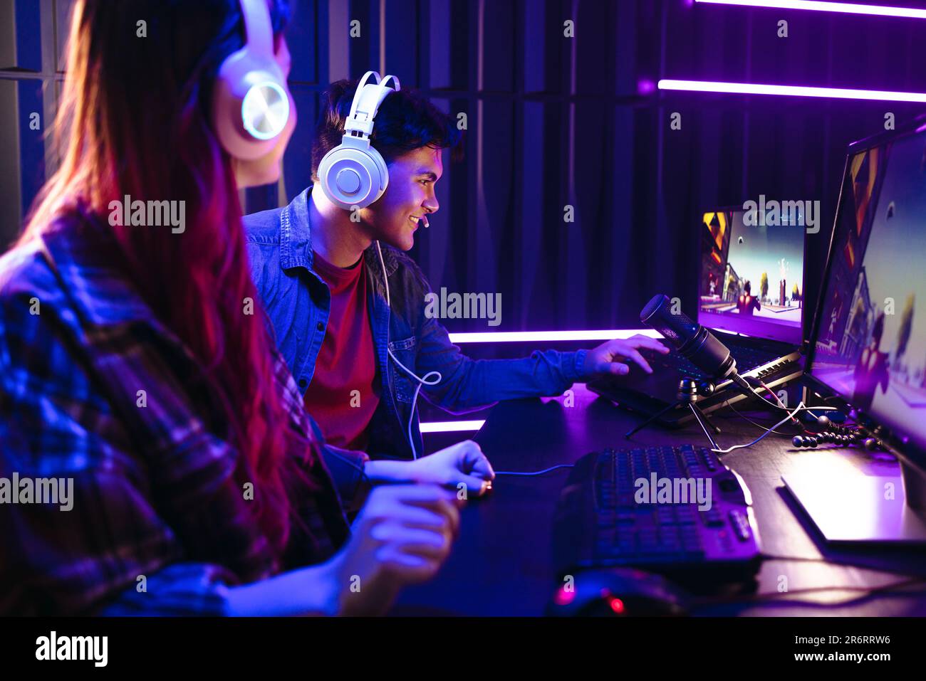 Due giovani giocatori, un uomo e una donna, si impegnano in un concorso di gioco su una piattaforma di gioco virtuale. Seduto di fronte a una configurazione multi monitor, Young Gen Z g Foto Stock