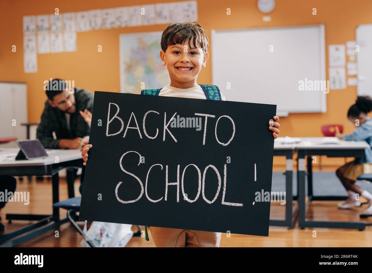 Bambino eccitato pronto per il primo giorno di scolarizzazione co-ed ed apprendimento permanente. Ragazzo felice in piedi in classe con un cartello di ritorno a scuola. Elemen Foto Stock