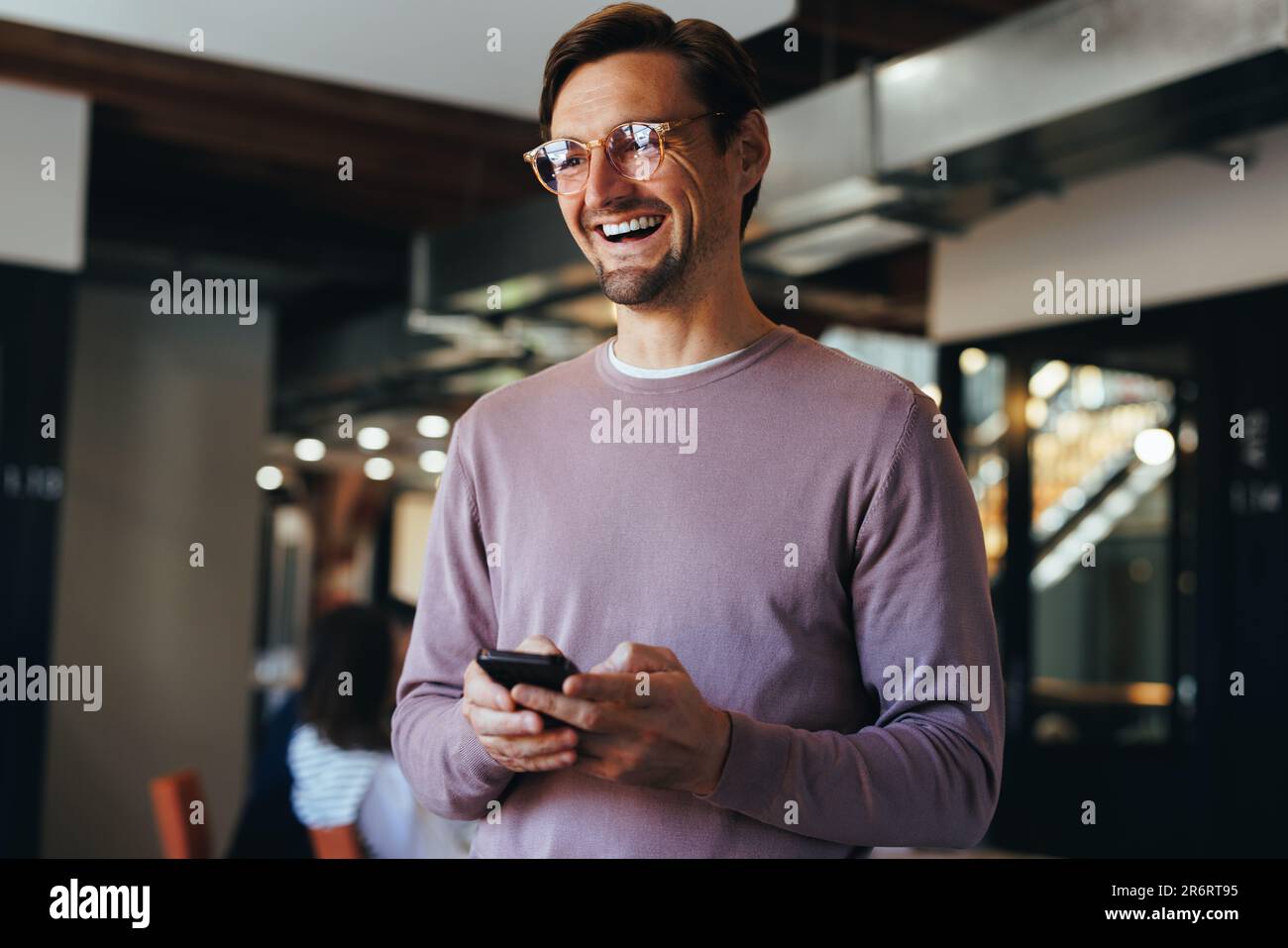 Professionista di sesso maschile che tiene un telefono cellulare mentre si trova in ufficio. Buon uomo d'affari che utilizza un cellulare per inviare un messaggio di testo in un moderno workplac Foto Stock