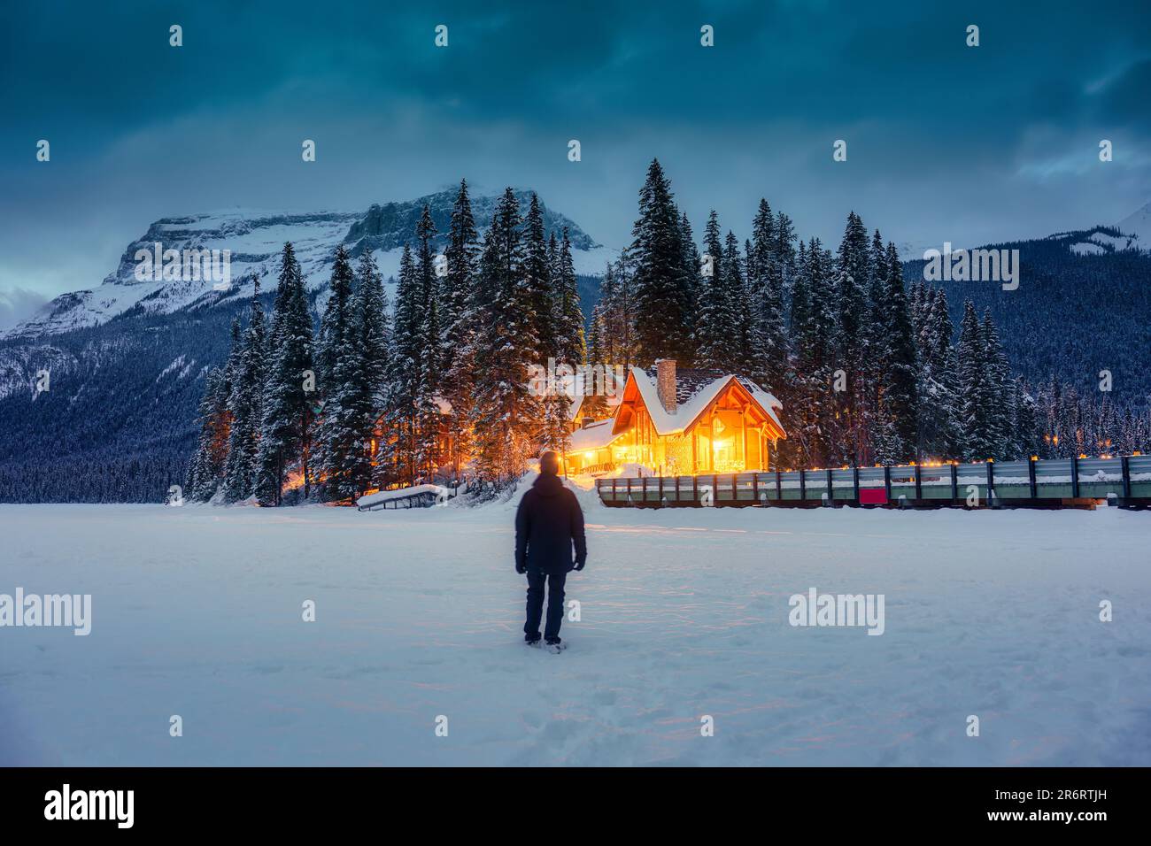 Un viaggiatore in piedi in campo di neve con loggia di legno incandescente e pineta in montagne rocciose al parco nazionale di Yoho, Alberta, Canada Foto Stock
