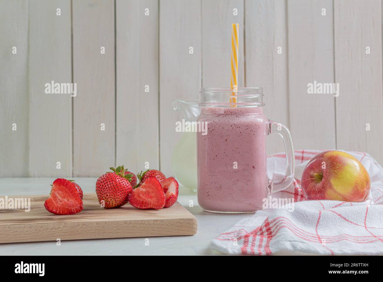 Milkshake fresco con fragole. Un bicchiere di frullato di fragole fresche. Purea di fragole fresche su uno sfondo di legno chiaro. Cibi e bevande sani Foto Stock