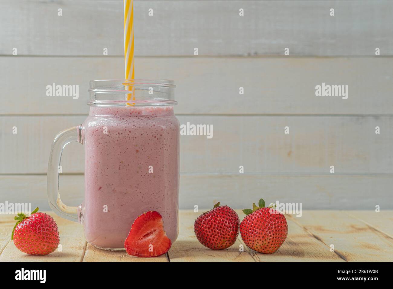 Milkshake fresco con fragole. Un bicchiere di frullato di fragole fresche. Purea di fragole fresche su uno sfondo di legno chiaro. Cibi e bevande sani Foto Stock