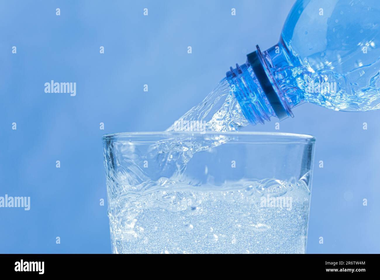 L'acqua fredda fluisce dal biberon al bicchiere. Versare l'acqua da una  bottiglia in un bicchiere su sfondo blu. Posiziona per testo Foto stock -  Alamy
