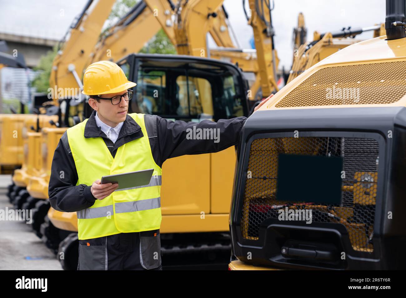 Ingegnere in un casco con un tablet digitale stand accanto agli escavatori da cantiere Foto Stock